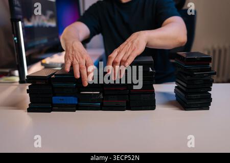 Person stacking multiple external hard drives on desk, creating organized piles for secure data management, archiving, digital asset backup in home Stock Photo