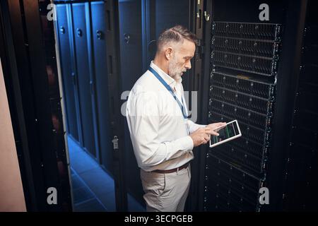 Tablet, man and technician in data center with inspection, research or programming on app. Cybersecurity, database and mature engineer in server room Stock Photo