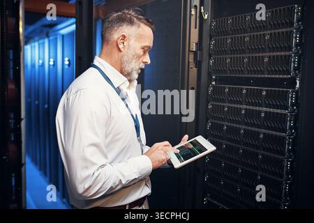 Tablet, man and engineer in data center with inspection, research or programming on app. Cybersecurity, database and mature technician in server room Stock Photo