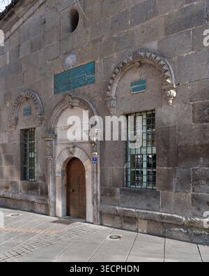 Historic stone facade of the Tomb of Zeynel Abidin in Kayseri, Turkey, featuring an arched wooden door, barred windows, and decorative calligraphic plaques Stock Photo