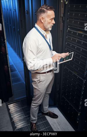 Tablet, man and programmer in data center with inspection, research or engineer on app. Cybersecurity, database and mature technician in server room Stock Photo