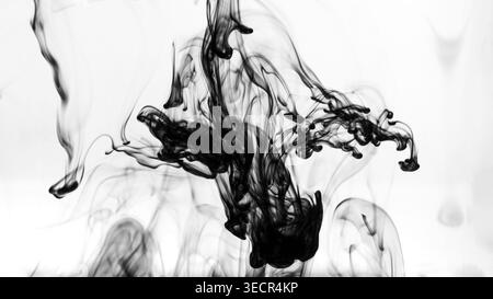 Black ink dissolving and creating abstract shapes and smoke-like patterns in water Stock Photo