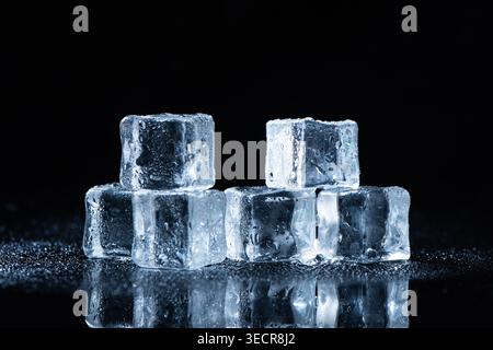 Frozen ice cubes with water droplets reflecting on a wet black surface Stock Photo