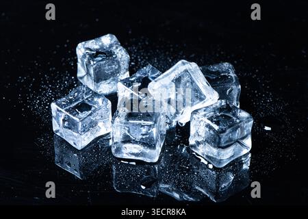 Ice cubes melting on a reflective black surface creating water drops Stock Photo