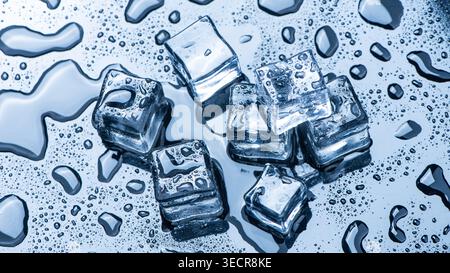 Ice cubes melting, forming water drops and condensation on a blue reflective surface Stock Photo