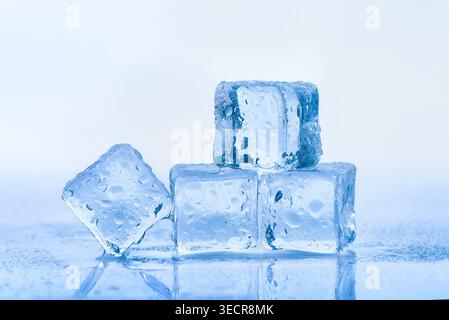 Ice cubes melting on a reflective surface, creating water droplets Stock Photo