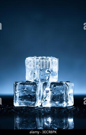 Three clear ice cubes with water drops reflecting on a dark surface Stock Photo