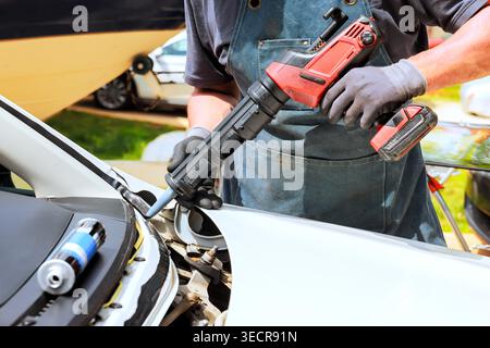 Handy man works on car using power tool workshop has various vehicles in background. Stock Photo