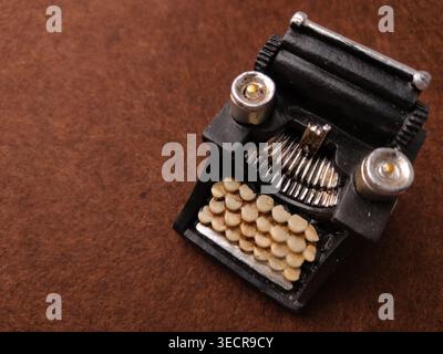A detailed miniature black typewriter sits on a brown textured surface, showing keys and a carriage. Stock Photo