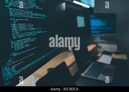 Close up of computer monitors displaying source code in a modern workstation with laptop and digital devices, showing software development workflow, p Stock Photo
