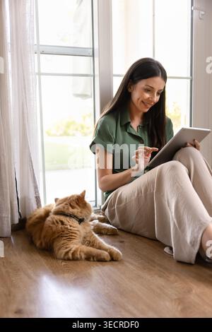 Woman using tablet sitting on floor with cat Stock Photo