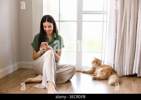 Woman using smartphone while sitting on floor with cat Stock Photo