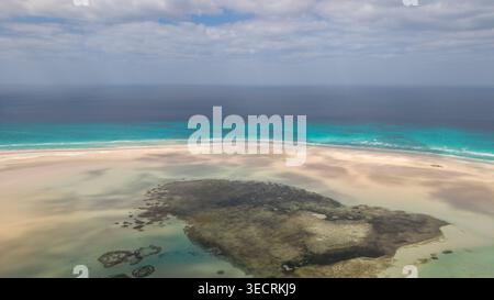 Aerial view of tropical sandbar and shallow lagoon with turquoise ocean, coral reef textures, and cloudy sky on horizon. serene seascape background. D Stock Photo