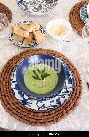 Aesthetic Mediterranean Table Setting with Asparagus Soup. Traditional blue white floral porcelain on natural woven placemats highlights modern rustic Stock Photo