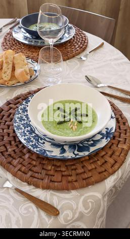 Creamy Asparagus Soup in Mediterranean Table Setting. Sustainable dining trend features organic green soup served on handcrafted natural fiber Stock Photo