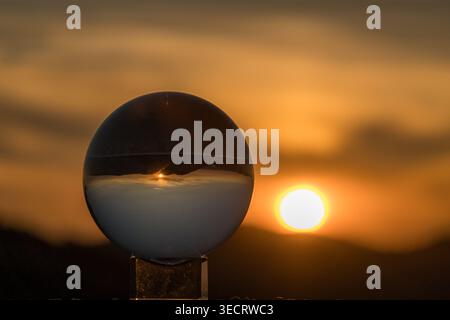 A mesmerizing scene captures the golden hour as the sun sets, its warm light reflecting through a crystal ball, creating an enchanting play of sunligh Stock Photo