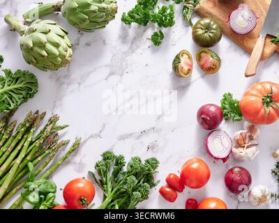 Various types of vegetables are placed on a marble kitchen countertop. The arrangement includes leafy greens, tomatoes, onions, and more, highlighting Stock Photo