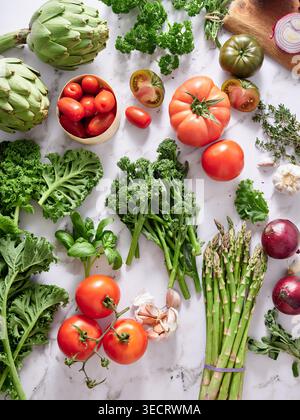 Various vegetables are neatly arranged on a marble kitchen countertop. There are tomatoes, greens, and other fresh ingredients ready for cooking. This Stock Photo