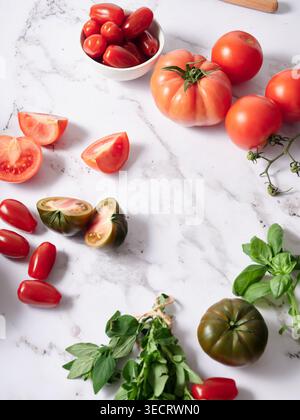 Various fresh vegetables are arranged on a marble kitchen countertop. Bright red tomatoes and green herbs fill the space. This scene shows healthy ing Stock Photo