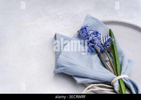 Delicate blue hyacinth flowers wrapped in pale linen and tied with twine, arranged on a light tabletop. Minimal interior still life with airy space an Stock Photo