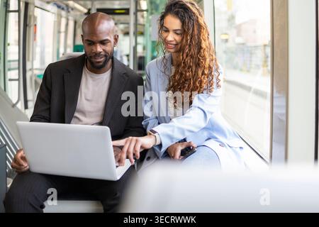 Business couple on a work trip uses a laptop and smartphone on a modern train, reviewing plans and documents together during commute for mobile teamwo Stock Photo