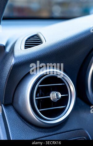 Close-up of a modern car interior showing a circular air vent with chrome trim set in a textured black dashboard, highlighting automotive design, comf Stock Photo