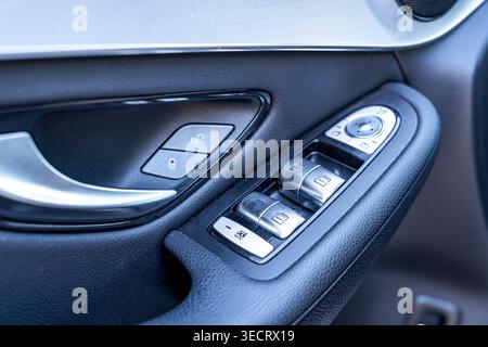 Detailed close-up of a modern car door interior featuring electric window switches, mirror adjustment control, and door lock buttons on textured black Stock Photo