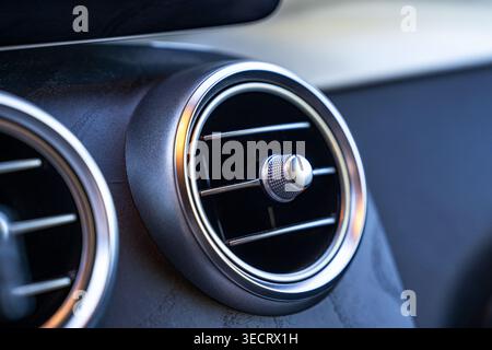 Macro close-up of a modern car air vent with metallic trim and control knob on a black dashboard, highlighting interior design, ventilation, and autom Stock Photo
