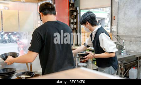 Two chefs work in a Taiwanese restaurant kitchen, preparing traditional dishes like xiaolongbao. The vibrant setting showcases authentic culinary tech Stock Photo