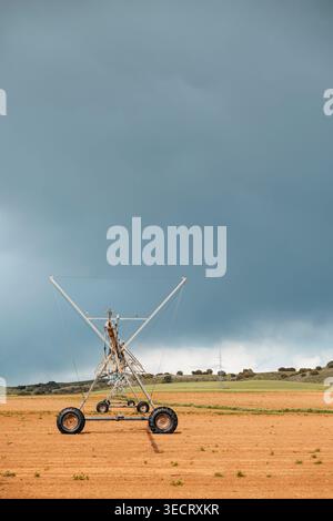 Center pivot irrigation machine stands on a dry harvested field, stretching across open farmland as dark storm clouds gather, showing agriculture and Stock Photo