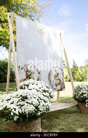 Rustic Easter lunch on a sunny farm, featuring a bunny welcome sign on an easel, wicker baskets of daisies, and a cheerful outdoor setup for a surpris Stock Photo