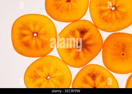 Bright orange persimmon slices arranged as a seamless fruit background, close-up macro texture with soft light, minimal design for fresh food, health Stock Photo