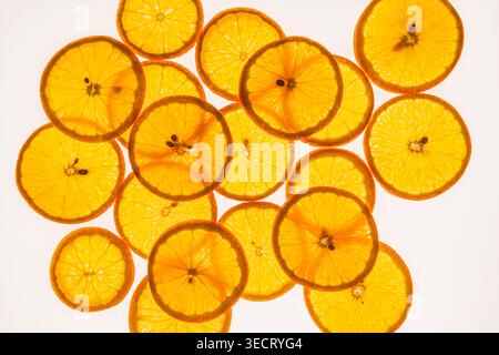 Bright backlit orange slices arranged in an overlapping pattern on a clean white background, highlighting citrus texture, freshness, and vibrant color Stock Photo