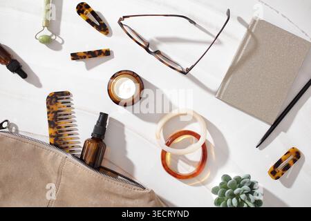 Styled composition of cosmetic products, hair accessories, and notebook on a marble background, capturing a soft feminine aesthetic and slow beauty li Stock Photo