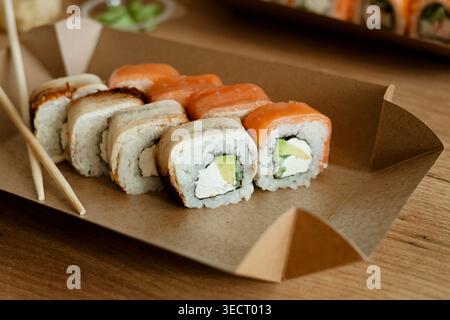 A delicious assortment of sushi rolls served on a paper tray, accompanied by chopsticks, set on a wooden table. Perfect meal for a relaxing day off at Stock Photo