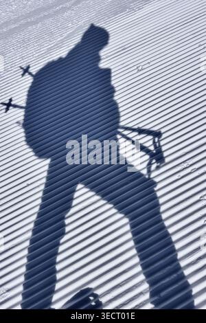 The shadow of a skier with poles is cast on a perfectly grooved snowy surface, creating a striking visual contrast between light and shadow in a winte Stock Photo