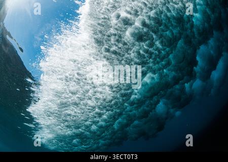 Underwater close-up of a powerful ocean wave breaking overhead, with swirling turquoise water, frothy bubbles, and sunlight filtering through in a dra Stock Photo