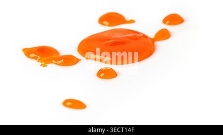 Bright orange liquid dripping and pooling on a clean white surface Stock Photo