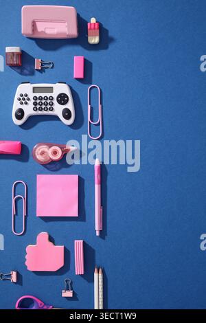Pop art flat lay of pink school supplies on blue background with a gamepad shaped calculator, sticky notes, clips, pencils and pen, blending Gen Z gam Stock Photo