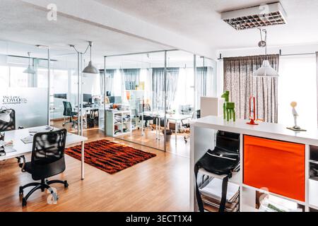 Bright modern open plan office with glass partition walls, desks and chairs, pendant lights, wooden floor and minimalist decor in a contemporary works Stock Photo