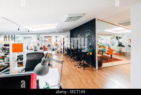 Bright modern open plan office interior with desks, computers and chairs, featuring a black chalkboard wall for brainstorming and a glass meeting room Stock Photo