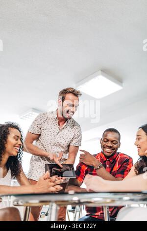 Diverse coworkers share ideas in a bright office meeting, laughing and collaborating around a table while one colleague shows results on a tablet scre Stock Photo
