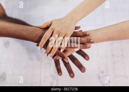 Close-up of diverse hands stacked together on a desk, symbolizing teamwork, inclusion, trust, and collaboration in a modern workplace or community pro Stock Photo