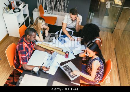 Overhead view of a diverse team collaborating at a conference table, using laptops and documents to plan a project in a modern office during a focused Stock Photo
