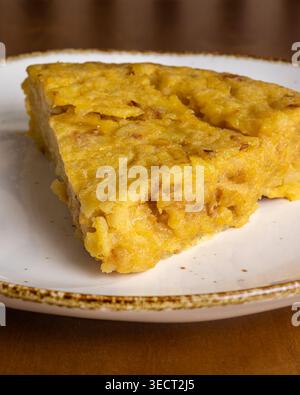 Close-up of a slice of Spanish tortilla with potato and egg served on a white plate, warm and hearty breakfast food photographed in soft morning light Stock Photo
