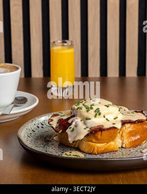 Appetizing morning breakfast on a cafe table with eggs benedict on toast topped with hollandaise and chives, served with hot coffee and fresh orange j Stock Photo