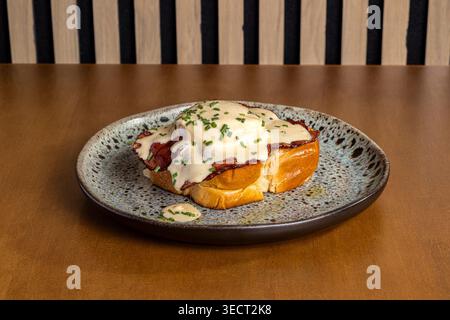 Close-up of eggs benedict topped with creamy hollandaise and chives on a toasted bun, served on a ceramic plate for a warm, savory morning breakfast. Stock Photo