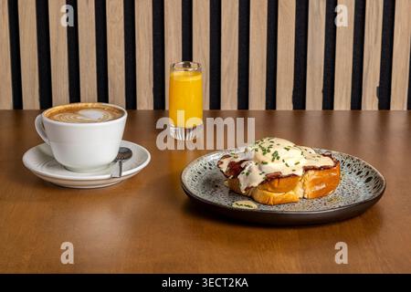 Morning breakfast on a café table with cappuccino in a cup, a small glass of orange juice, and eggs benedict on toasted brioche topped with hollandais Stock Photo