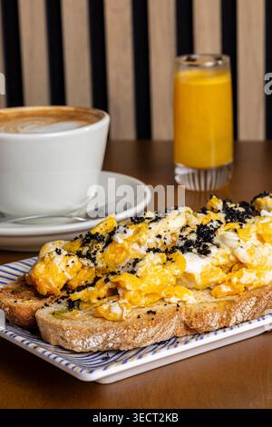 Hearty breakfast on a table featuring toast topped with scrambled eggs and seasoning, served with a cup of coffee and a glass of orange juice in a coz Stock Photo