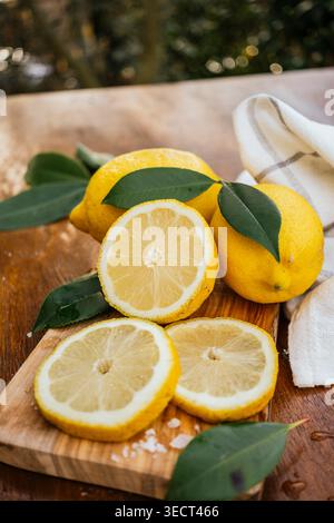 Fresh yellow lemons with green leaves and sliced citrus arranged on a wooden cutting board, natural light and soft bokeh background, healthy food and Stock Photo